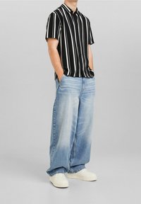 Svart och vitrandig kortärmad skjorta i kombination med ljusblå vida jeans och vita sneakers. Knappfrontdesign, avslappnad passform.