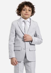 Completo grigio chiaro con giacca strutturata e pantaloni, dotato di due tasche frontali e una camicia bianca fresca sotto.