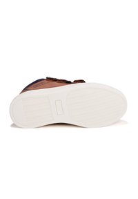 Braune Lederschuhe mit einer weißen Gummisohle, die ein strukturiertes Muster aufweist, und dunkelblauen Textilakzenten an der Ferse und den Riemen.