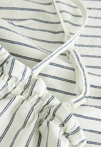 Tissu blanc avec de fines rayures horizontales bleu foncé, présentant un vêtement avec une taille élastique et un cordon de serrage assorti.
