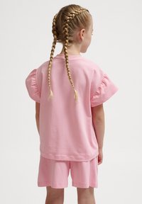 Rosa bomulls t-shirt med korta puffärmar och matchande shorts, i en avslappnad passform med slät textur. Bakifrån syns flätor.