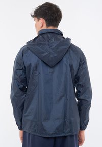 Giacca a vento blu navy con cappuccio, polsini elasticizzati e materiale leggero e lucido. Presenta un design semplice e lineare.