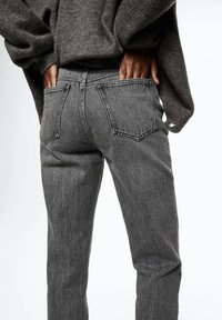 Jeans de mezclilla gris con una forma ajustada, bolsillos traseros y un acabado ligeramente desgastado, combinados con un suéter oscuro de corte oversize.