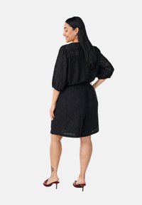 Vestido de tela de ojo de perdiz negro con mangas cortas, cintura ajustada y pantalones cortos. Presenta intrincados patrones de diamantes y un corte relajado.