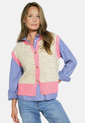 Knitted vest in cream and pink with horizontal stripes, featuring a button-down front, V-neck, and oversized armholes, worn over a blue striped shirt.