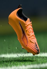 Scarpa da calcio arancione con tomaia testurizzata, dettagli neri e lacci prominenti. Progettata per le prestazioni su erba, con una struttura leggera.