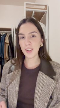 Blazer de espiga marrón y blanca con un cuello de cuero negro, utilizado sobre una blusa marrón. Pendientes circulares dorados visibles. Armario en el fondo.
