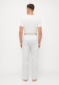 Witte crewneck t-shirt in combinatie met gestreepte, losse pyjamabroek. De broek heeft een elastische tailleband met een merklabel.