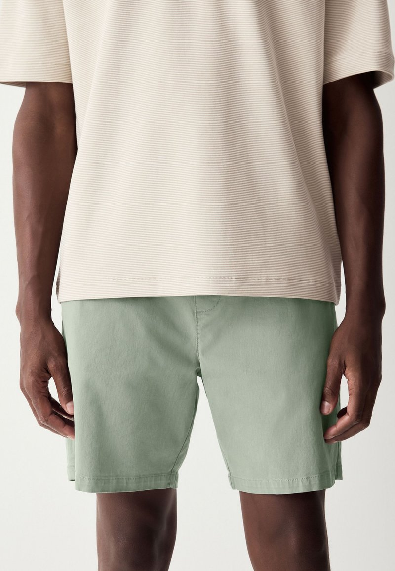 Chemise beige clair à manches courtes avec une texture côtelée subtile, associée à un short vert clair en tissu lisse et coupe droite.