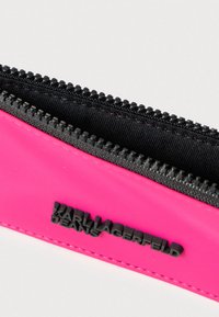 Ružové vrecko na zips z hladkého materiálu, s čiernym zipsom a vyrazeným logom "KARL LAGERFELD JEANS" na boku.