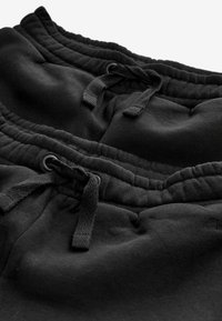 Zwarte sweatpants met een elastische tailleband, trekkoord en gestructureerde stof. Kenmerkt zich door stiksel-details en een klein logo nabij de zoom.