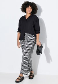 Chemise noire à boutons avec des manches retroussées, assortie à un pantalon large à carreaux noir et blanc. Sandales à plateforme noires et une pochette noire.