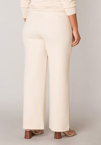 Beige wide-leg pants made of soft fabric, featuring a back pocket detail and clean lines. Paired with light brown block-heeled sandals.