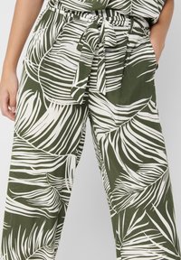 Groene wijde broek met een wit bladerenpatroon, voorzien van een tailleriem, zachte stof en zijzakken. Gladde textuur met een ontspannen pasvorm.