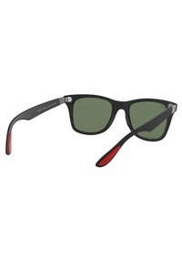 Occhiali da sole in plastica nera con lenti verdi, forma rettangolare e accenti rossi sulle tempie. Include componenti in metallo per la funzionalità delle cerniere.