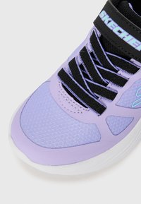 Baskets Skechers avec une tige en maille violet clair, des lacets noirs et une semelle extérieure blanche. Logo notable sur la sangle et découpes géométriques.