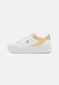 Białe sneakersy z gładką skórzaną cholewką, złotymi akcentami po bokach, białą gumową podeszwą oraz detalami logo na zewnętrznej stronie.