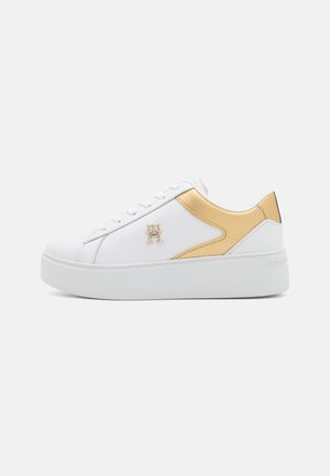 Białe sneakersy z gładką skórzaną cholewką, złotymi akcentami po bokach, białą gumową podeszwą oraz detalami logo na zewnętrznej stronie.