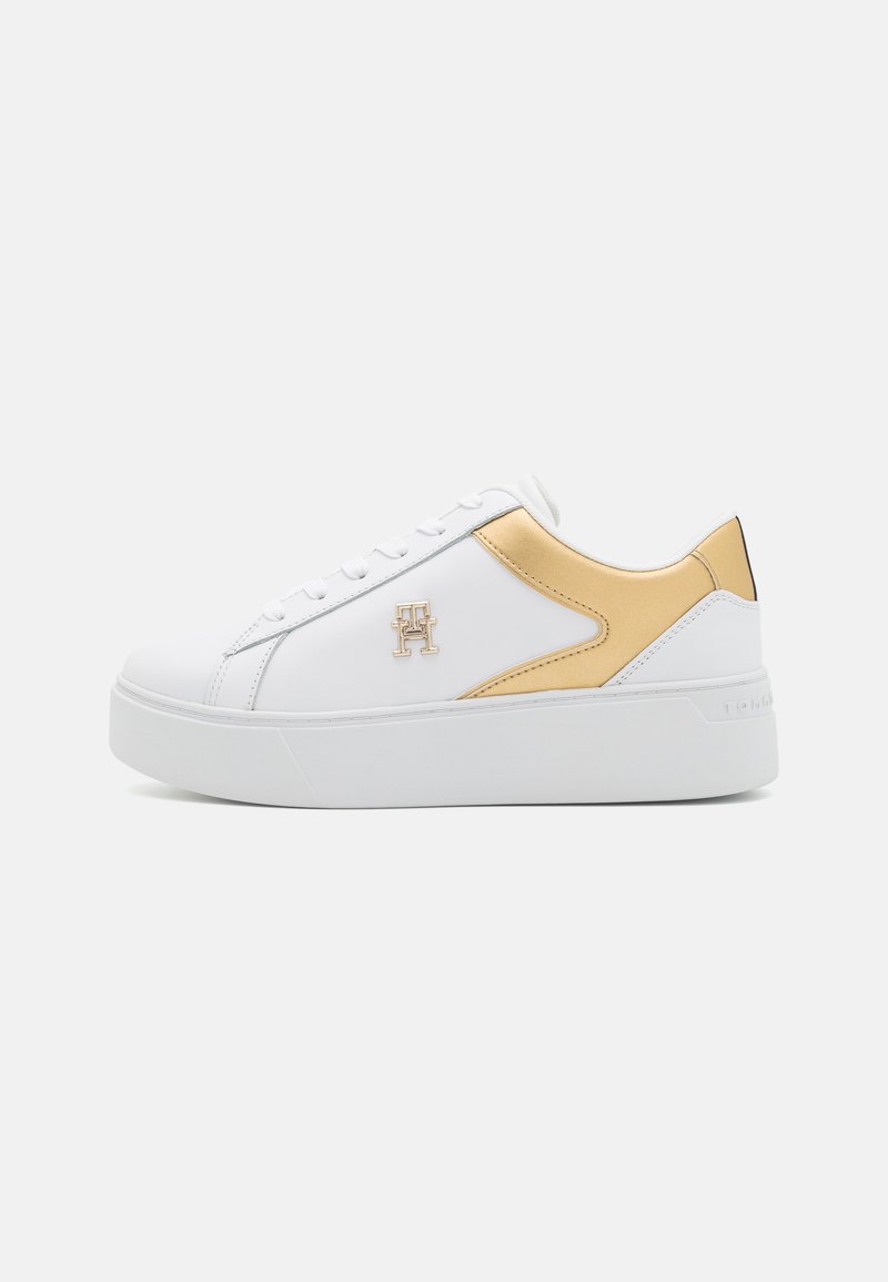 Białe sneakersy z gładką skórzaną cholewką, złotymi akcentami po bokach, białą gumową podeszwą oraz detalami logo na zewnętrznej stronie.