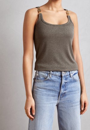 Femme portant un haut marron scintillant sans manches avec des bretelles en chaîne dorée, associé à un jean taille haute bleu clair.