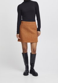 Gonna mini marrone con texture, dal design aderente e tasche anteriori, abbinata a un dolcevita nero a maniche lunghe e stivali neri lucidi al ginocchio.