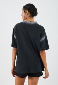 Sort oversize t-shirt med rund hals, korte ærmer og teksturerede detaljer. Fitted med en løs silhuet, parret med sorte shorts.