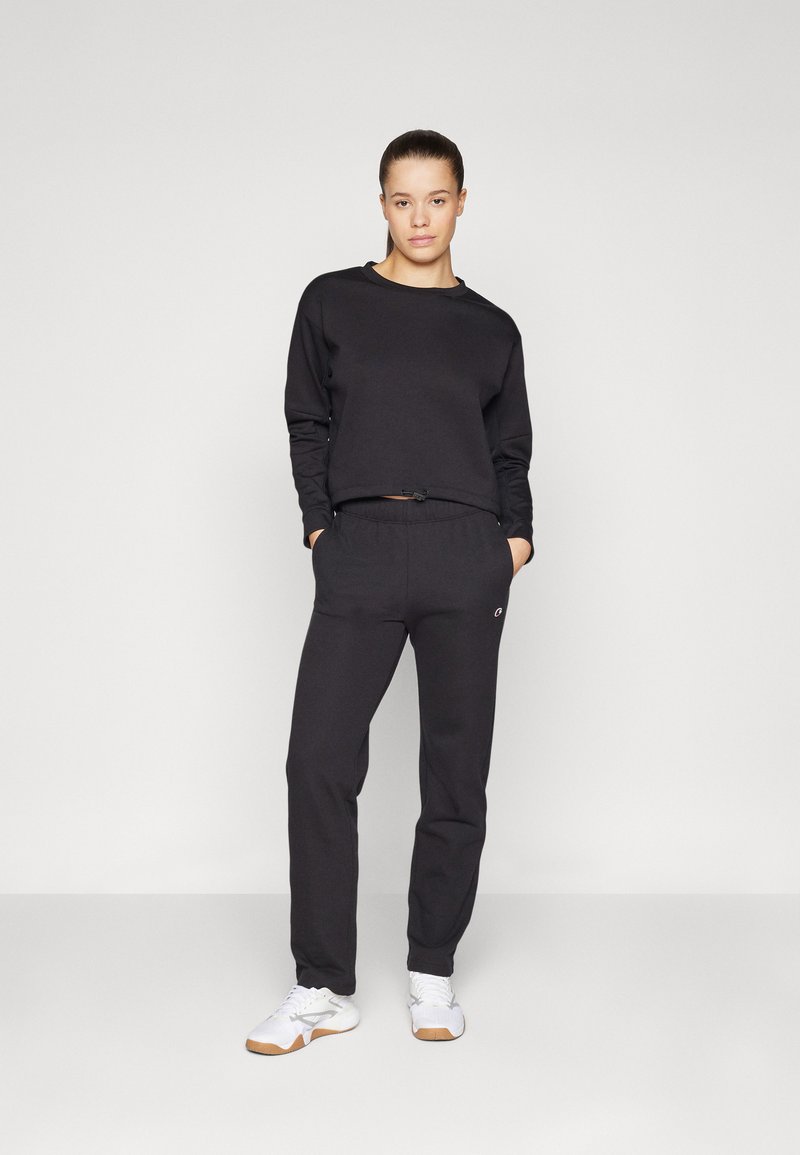 Felpa nera corta e pantaloni jogger abbinati, realizzati in tessuto morbido. Presentano una vita con coulisse e tasche laterali. Completati da sneakers bianche.
