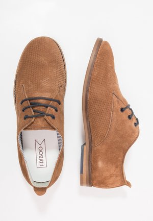 Paire de chaussures à lacets en daim marron avec détails texturés, lacets noirs et petit talon, vues de dessus et de profil.