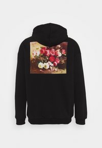 Sudadera negra con un gran diseño impreso de un arreglo floral en colores rosa, rojo y blanco en la parte posterior. Tejido suave, corte relajado.