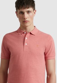 Korte mouwen polo shirt in lichtrood, van een katoenmix stof. Heeft een kraag, een drie knoopsluiting en een klein geel geborduurd logo.