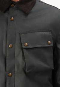 Zwarte button-up shirt met een corduroy kraag, voorzien van bronzen knopen en een borstzak. Gladde textuur, licht glanzende afwerking.