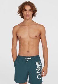Shorts de bain teal avec taille à cordon et poches lat�érales. Présente un grand logo blanc imprimé sur la jambe gauche. Texture lisse.