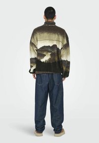 Fleece pullover with landscape print in brown, beige, and green; features a high collar and loose fit. Worn with dark blue denim pants.