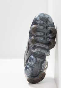 Suola di scarpa sportiva caratterizzata da un materiale testurizzato in nero e grigio, con elementi di ammortizzazione trasparenti e modelli di trazione distintivi.