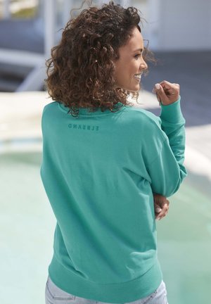 Turquoise sweatshirt with ribbed cuffs and hem. Features "ELBSAND" text printed at the back. Soft fabric with a relaxed fit.