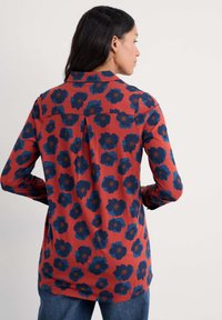 Koszula z długim rękawem, w kolorze czerwonym z ciemnoniebieskim kwiatowym wzorem. Posiada wykładany kołnierzyk oraz zakładki na plecach. Miękka tekstura materiału.