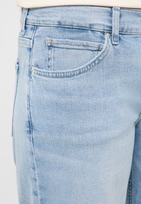 Svetlomodré rifle z denimu s prednými vreckami, pútkami na opasok a malým kovovým emblémom koňa na mincovom vrecku.