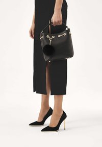 Mustast nahast ämbrikujuline kott tekstuurse viimistlusega, kullast kettdetailide ja eemaldatava musta pompomiga. Koos mustade seemisnahast kontsakingadega.