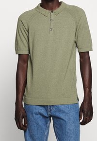 Olivově zelená polokošile s krátkým rukávem z texturované pleteniny, s límečkem a tříknoflíkovou légou. Volný střih.