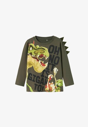 T-shirt à manches longues vert avec un grand graphique de dinosaure, un texte audacieux et des appliqués en forme de pic sur l'épaule. Tissu doux, design décontracté.