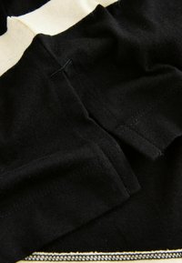 Mustast kangast, sileda tekstuuriga, kreemika triibuga. Märkimisväärsed õmblusdetailid ja selgelt eristuv äärepidi detail.