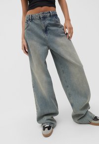 Vaaleansininen denim leveälahkeinen farkut korkealla vyötäröllä, joissa on etutaskut ja hillitty haalistus, yhdistettynä harmaisiin ja mustiin kenkiin.
