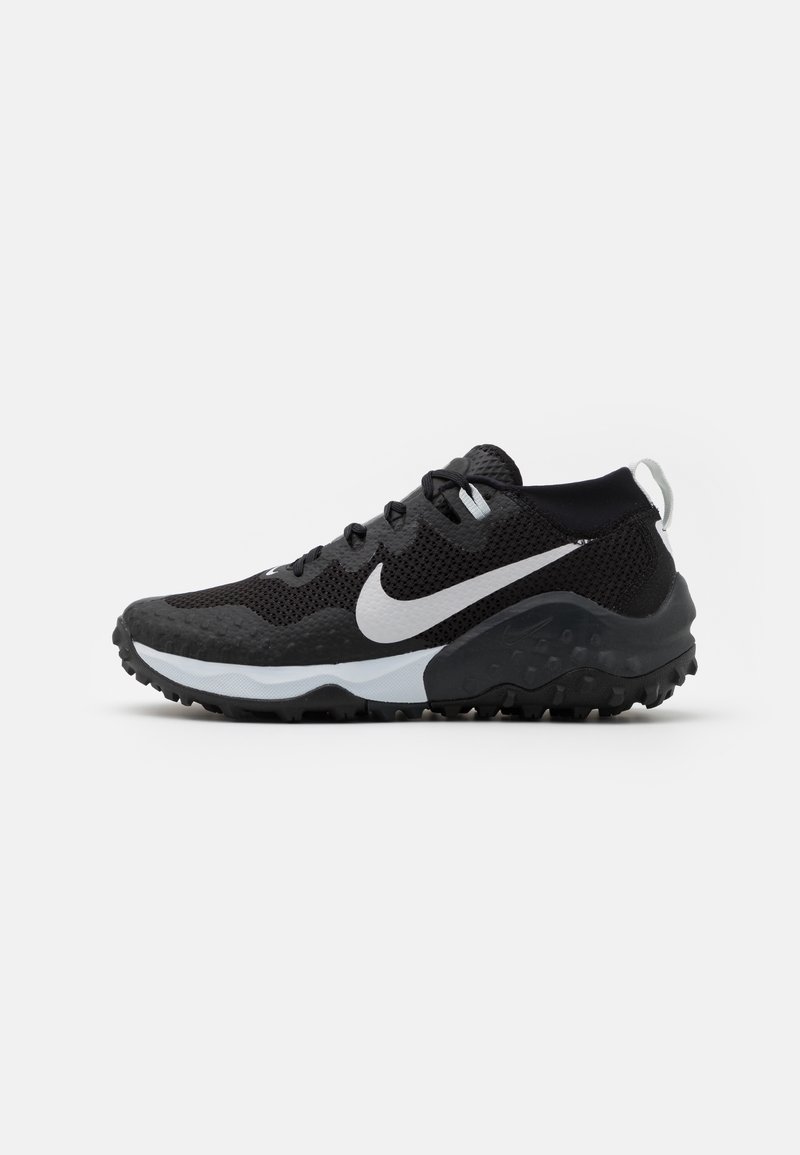 Chaussure de sport noire et blanche avec tige en mesh, semelle texturée, lacets et logo Nike swoosh blanc sur un fond uni.