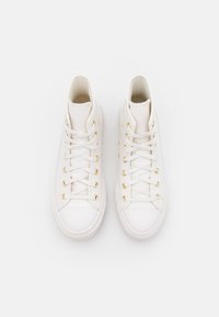White high-top sneakers made of smooth leather, featuring gold eyelets, white laces, and a rounded toe design.