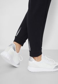 Zwarte sportieve joggingbroeken met reflecterende accenten op de manchetten, gecombineerd met witte gestructureerde sneakers met zilveren details en een gevoerde zool.