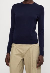 Maglione lavorato a maglia blu navy, colletto rotondo, maniche lunghe, orlo a coste, realizzato in materiale morbido, abbinato a pantaloni beige a gamba larga.