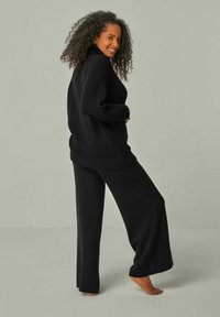 Schwarzer, übergroßer Pullover mit hohem Kragen und gerippten Bündchen, kombiniert mit weiten schwarzen Hosen. Weiche Textur, minimalistisches Design, keine Muster.