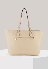 Beige læder tote taske med polerede metal accenter, der har to lange håndtag og en frontlomme med lynlås. Blød, tekstureret overflade.
