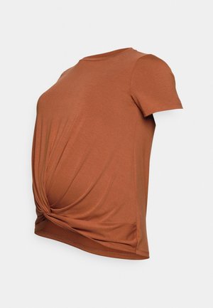 T-shirt de maternité à manches courtes couleur rouille avec détail torsadé à l'avant et tissu doux et extensible, présenté sur un fond uni.