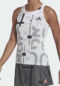 Vitt och svart mönstrat ärmlöst träningslinne med rund hals, gjort av lätt material, med en Adidas-logotyp på bröstet.